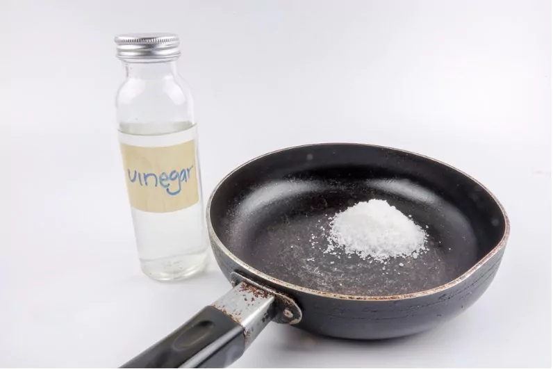 a cast iron pan with a bottle of vinegar and some salt