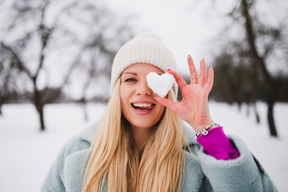 a girl holding heart shaped snow in front of her eye