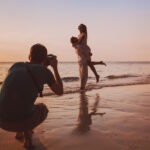 A photographer clicking photos of a couple on a beach.