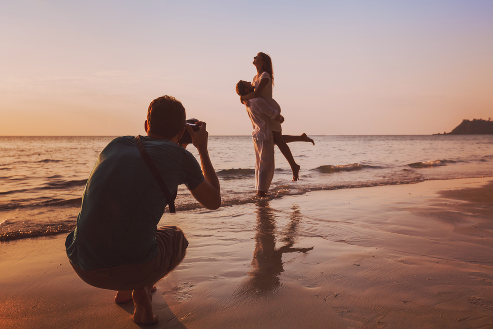 A photographer clicking photos of a couple on a beach.