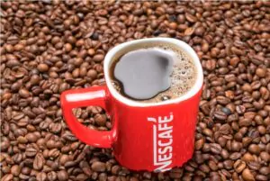 red mug of nescafe on the background of scattered coffee beans
