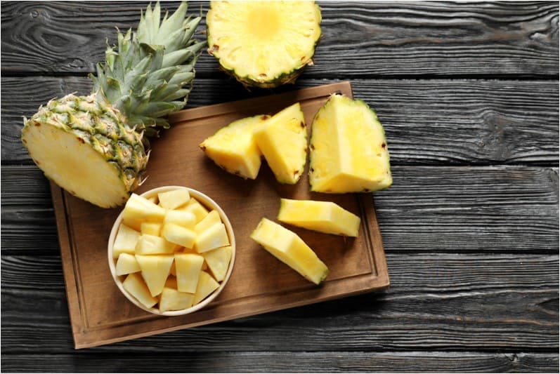 wooden board with fresh sliced pineapple on table