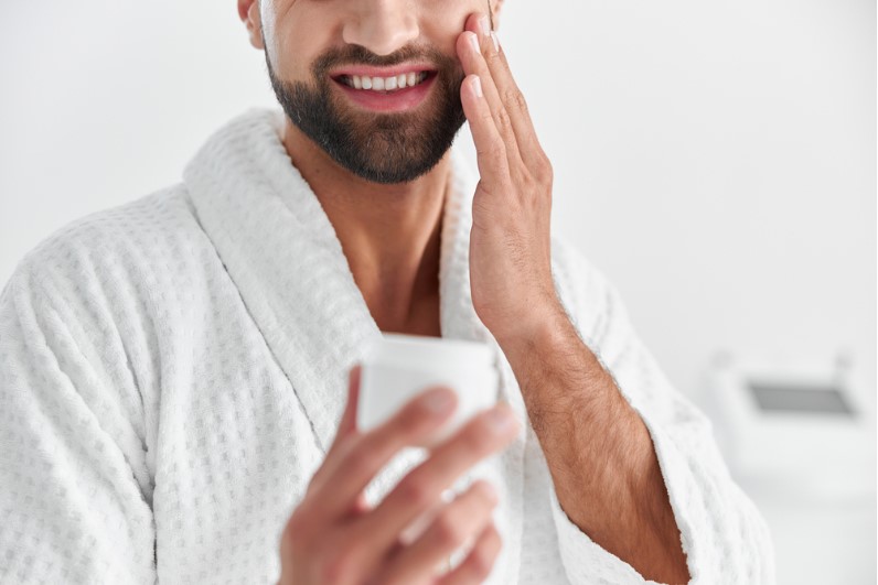 a cheerful bearded man in a bathrobe applying beard cream on beard