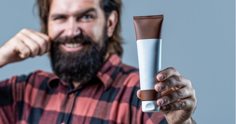 a man with beard holding a bottle of beard conditioner