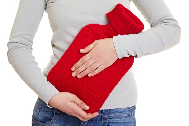 woman hands holding a red hot water bottle with cover for stomach ache