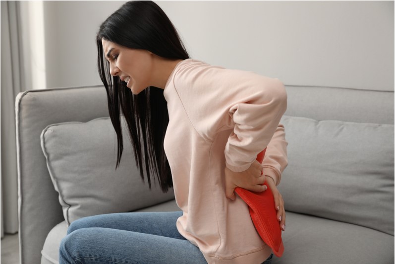 woman using hot water bottle to relieve low back pain on sofa at home