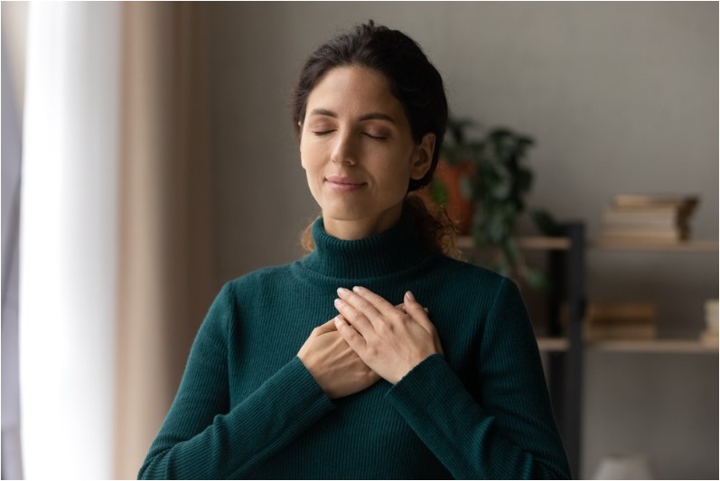 young attractive woman holding folded hands on chest praying and being grateful