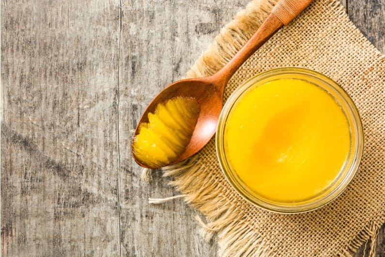 ghee or clarified butter in jar and wooden spoon on wooden table