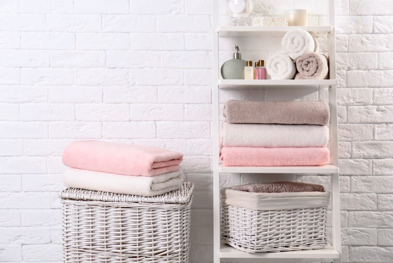 shelving unit and baskets with clean towels and toiletries near brick wall