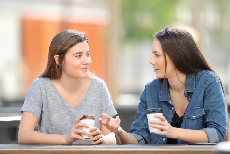 two casual friends talking in a park drinking coffee