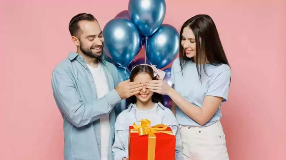young parents mom dad surprising their daughter with birthday gift and balloons