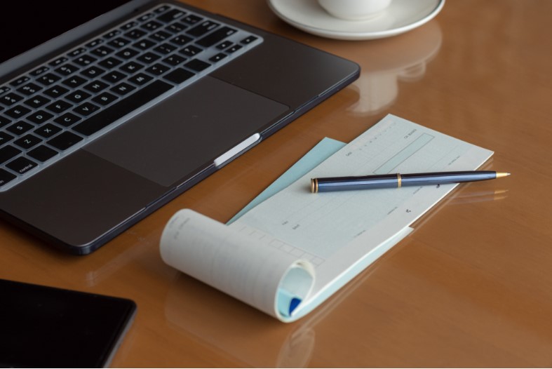 image of a laptop computer cheque book pen smartphone and cup of coffee on the wooden table