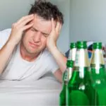 man suffering from a hangover holding his aching head with bottles of beer