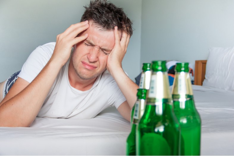 man suffering from a hangover holding his aching head with bottles of beer