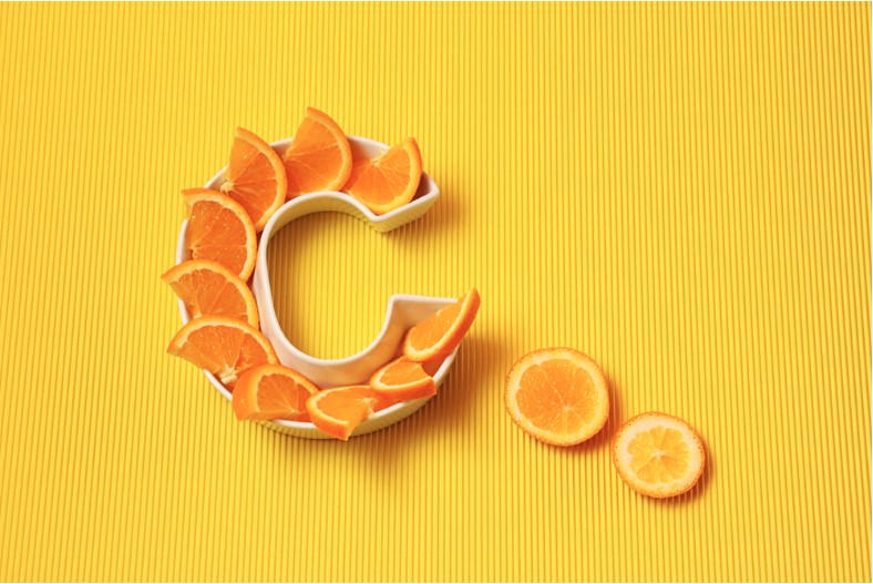 vitamin c in food concept. plate in the shape of letter C with orange slices on bright yellow background