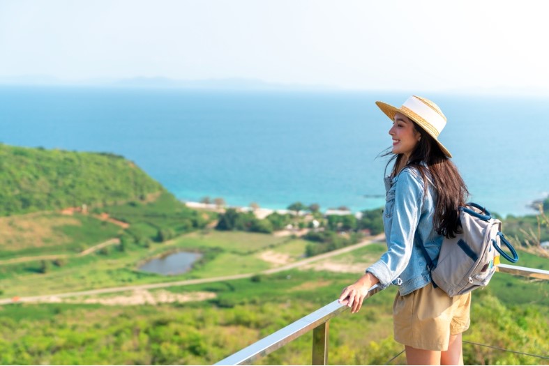 asian woman with backpack solo travel on tropical island mountain peak in summer sunny day