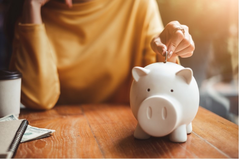 woman hand putting money coin into piggy for saving