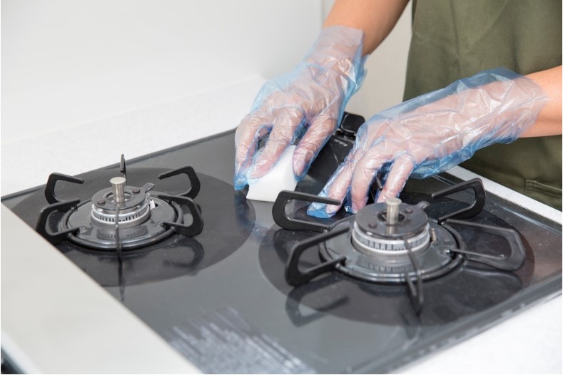 a woman cleaning the gas stove while wearing gloves in her hands