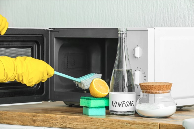 woman cleaning microwave oven with brush baking soda and vinegar at home