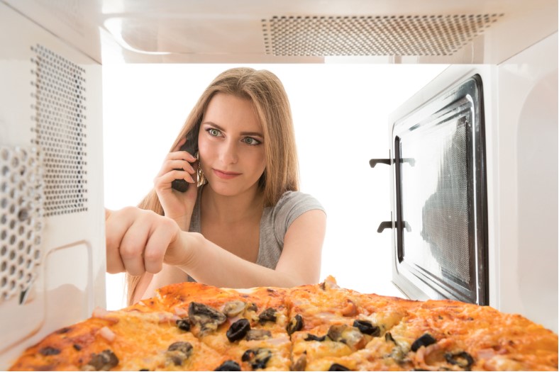 a girl looking at a pizza in the microwave