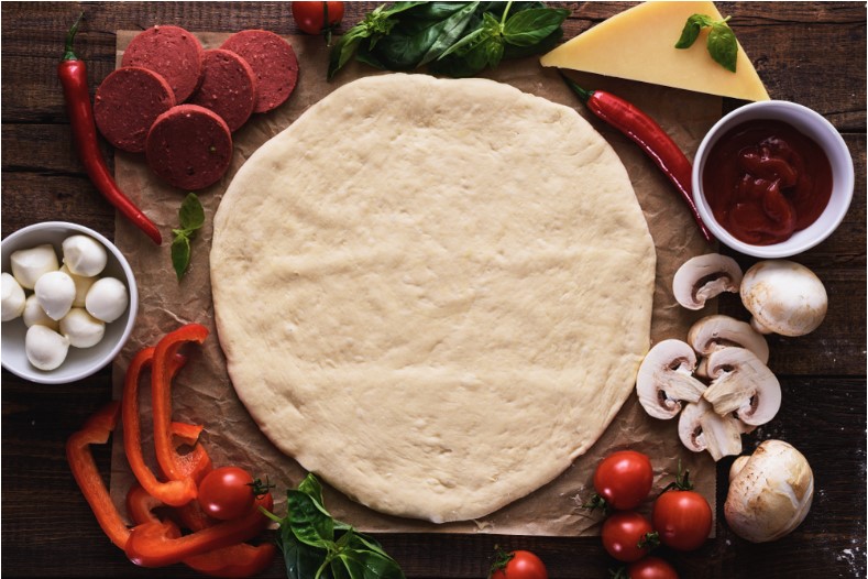 pizza base dough with ingredients on wooden background