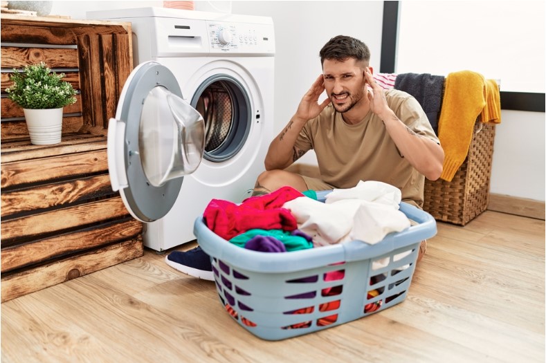 young man covering his ears due to loud noise from washing machine