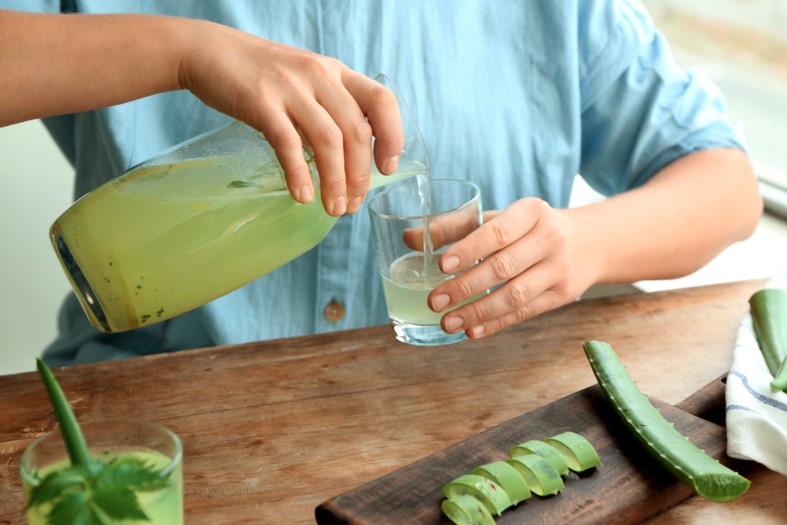 woman pouring aloe vera cocktail from jug into glass at wooden table
