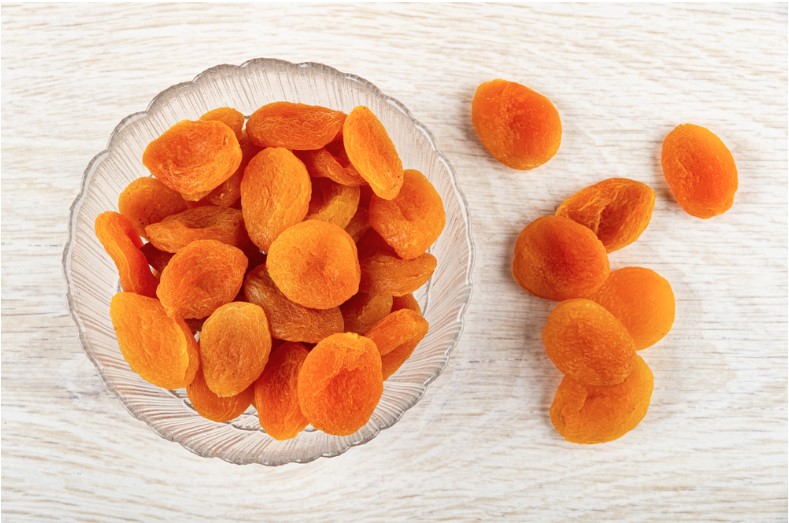 dried apricots in glass transparent bowl and on wooden table