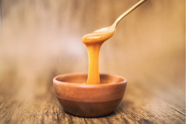 manuka honey spoon dipped in golden liquid natural superfood on wooden background