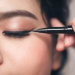 close up portrait of beautiful girl touching black eyeliner to her eyelid with closed eyes