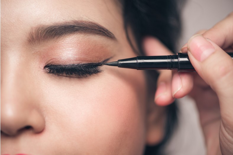 close up portrait of beautiful girl touching black eyeliner to her eyelid with closed eyes