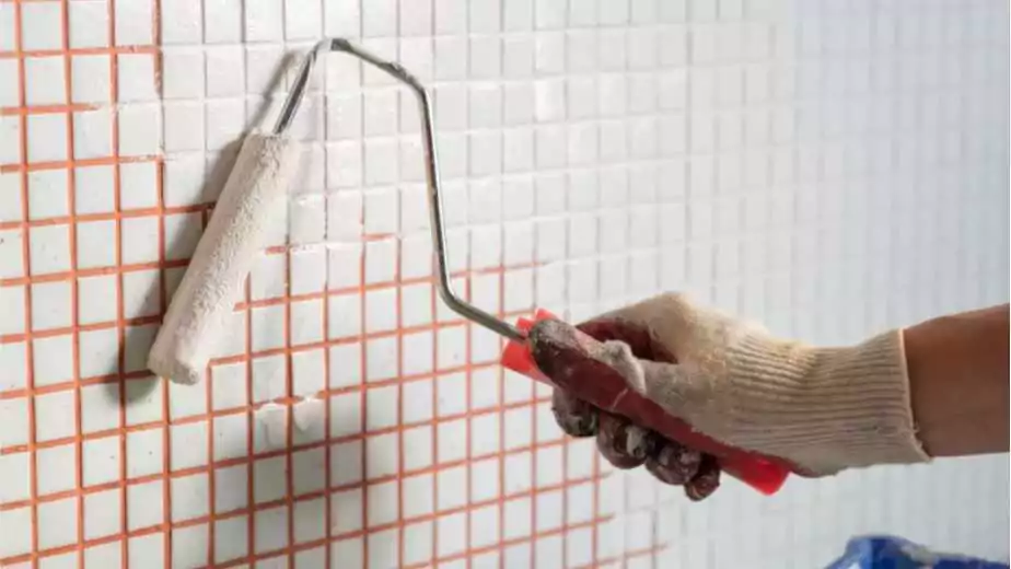 human hand holding paint roller over floor tile in the bathroom