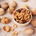 walnut kernels in a wooden bowl and whole walnuts on table