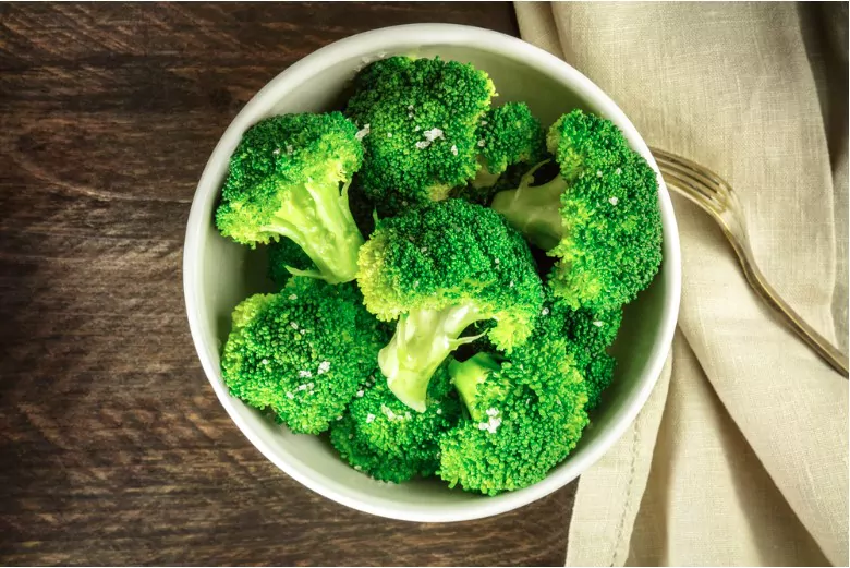a bowl of cooked green broccoli with sea salt