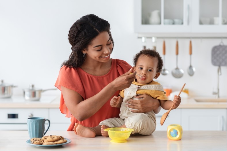 mother feeding little toddler son from spoon in kitchen