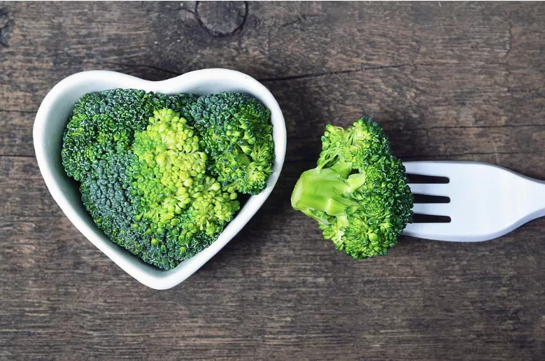 fresh raw broccoli in a white heart shaped bowl on old wooden rustic table