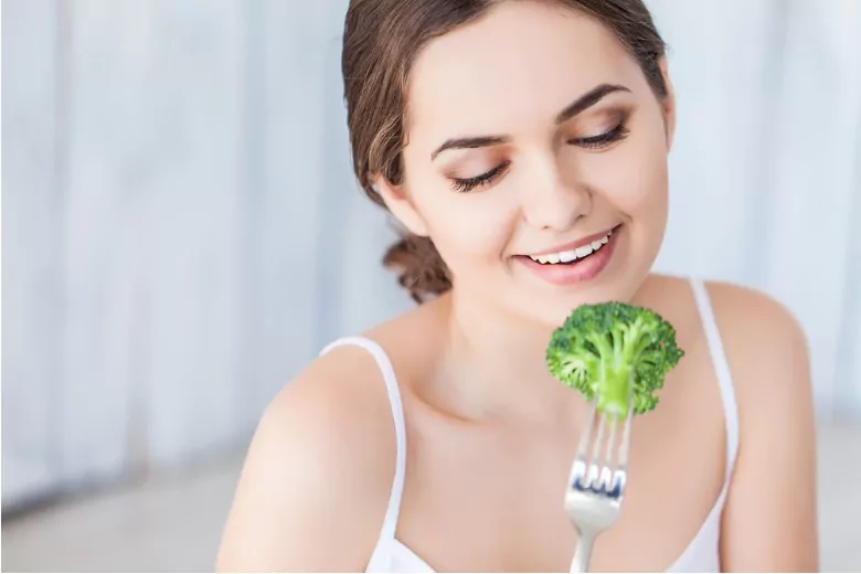 portrait of happy smiling young beautiful woman eating broccoli