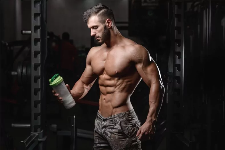 handsome athletic fitness man holding a protein shaker and posing gym