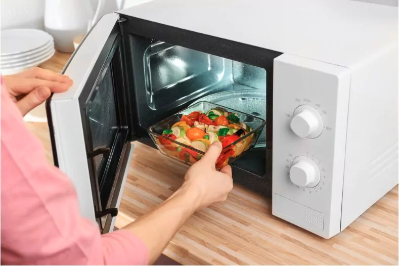 woman putting bowl with vegetables in microwave oven