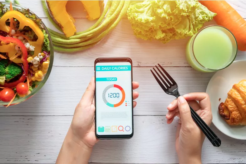 woman using calorie counter application on her smartphone at dining table with salad