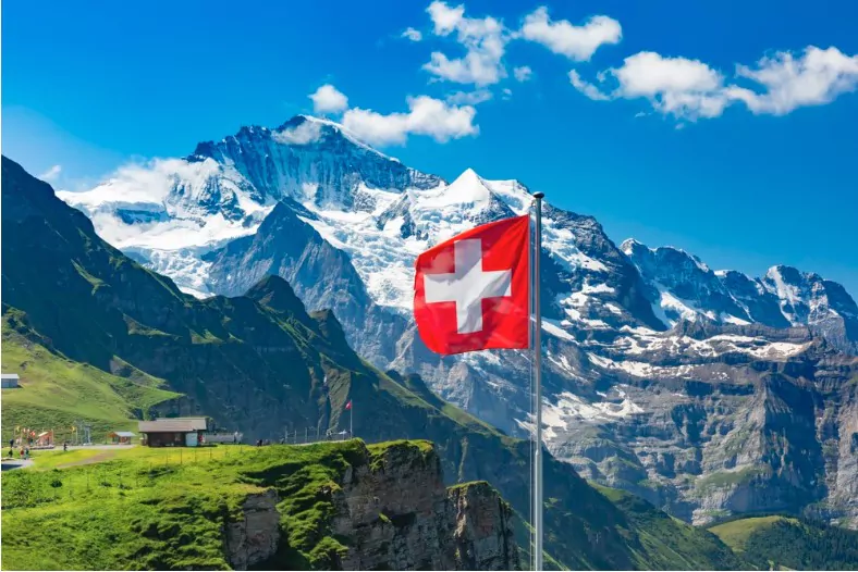 swiss flag waving at the peaks of monch and jungfrau mountains in switzerland