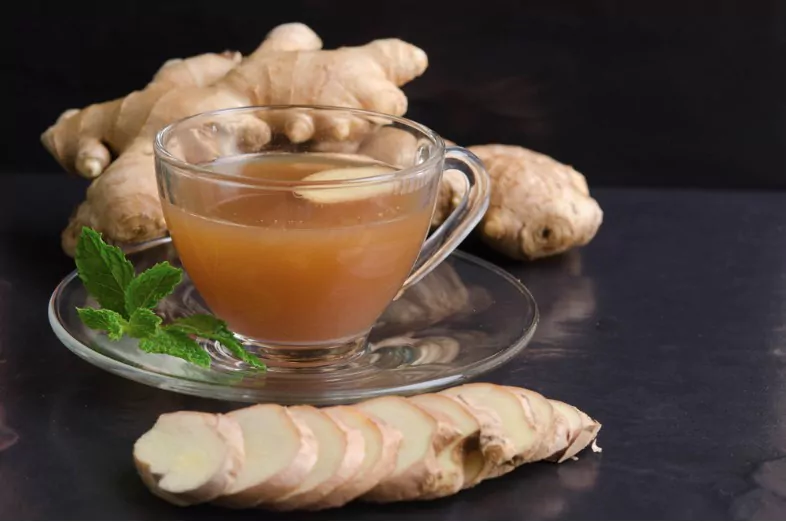 hot ginger water and mint with root and slices of ginger on black stone background
