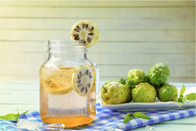 noni herbal juice and noni fruit in the dish on wooden background