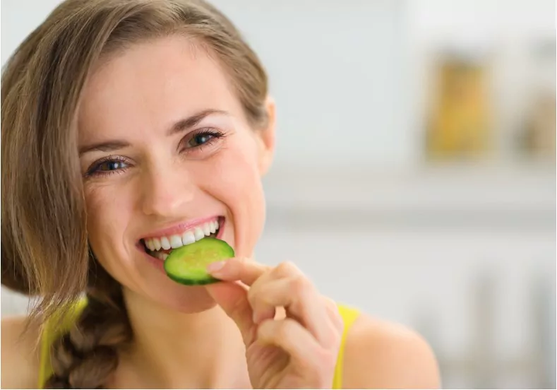 happy young woman eating slice of cucumber