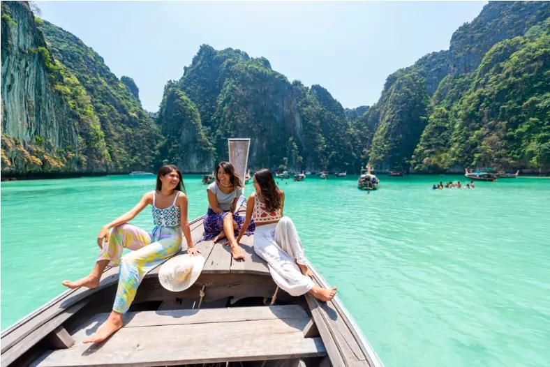 group of young asian woman friends sitting on the boat passing island beach lagoon in summer sunny day in thailand