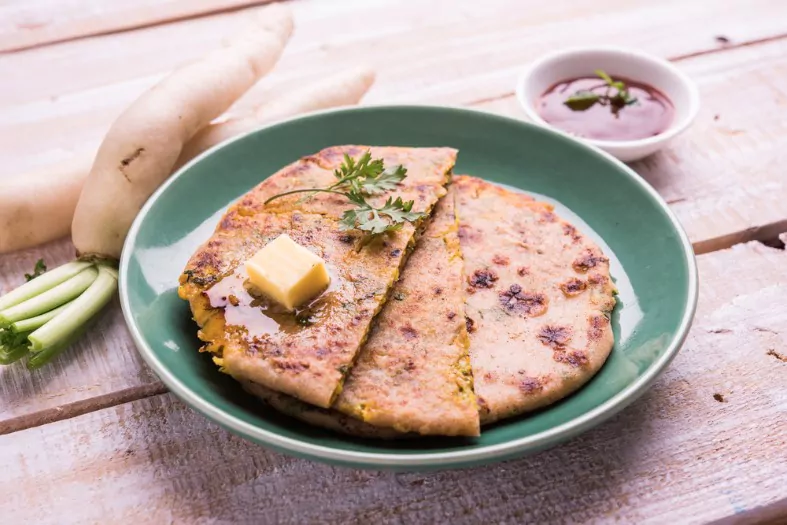 mooli stuffed paratha served in a plate with butter and tomato ketchup