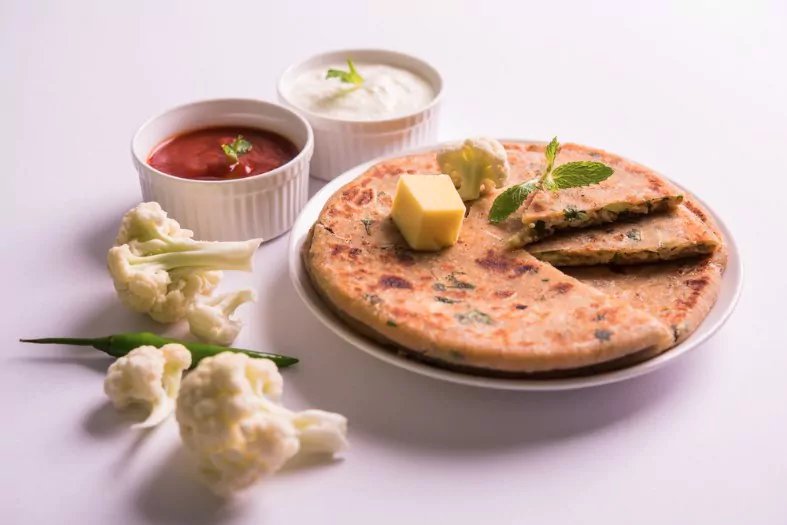 gobi paratha served over moody background with curd and tomato ketchup in bowl