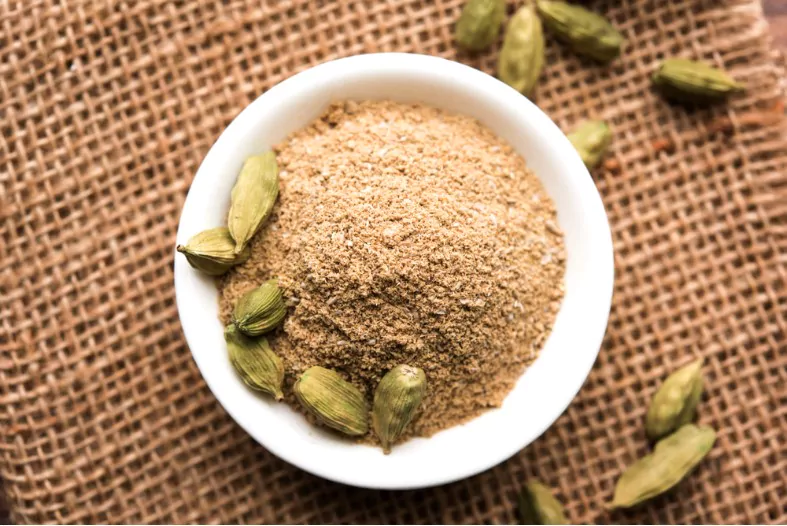 elaichi or cardamom powder in bowl or heap over moody background with pods