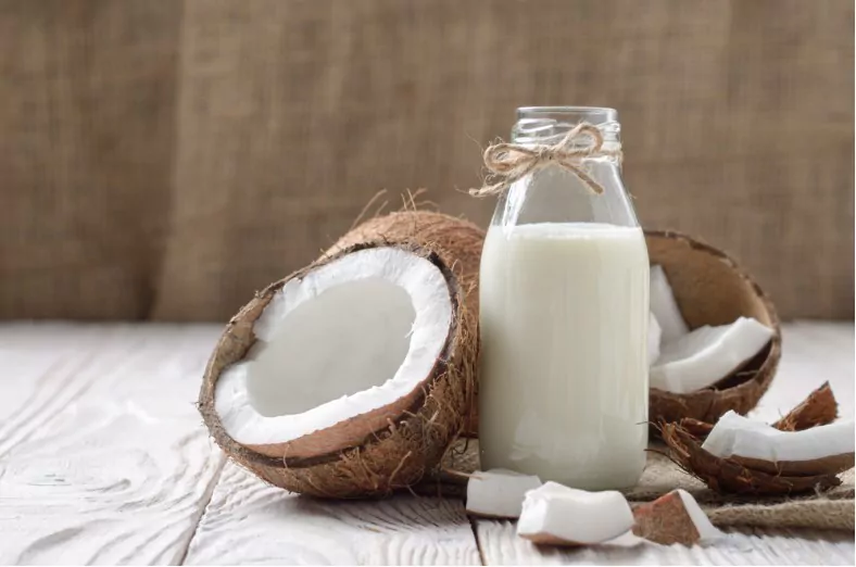 glass bottle of milk or yogurt on hemp napkin on white wooden table with coconut aside