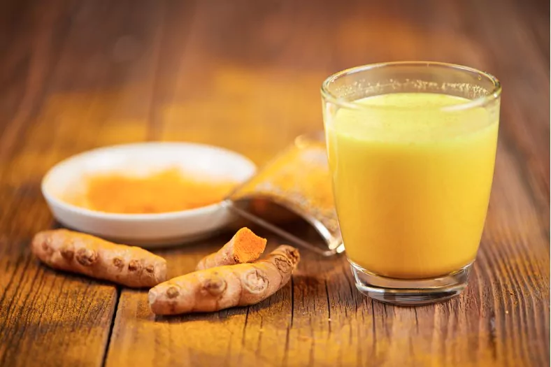 turmeric orange golden milk with root and powder on a wooden table